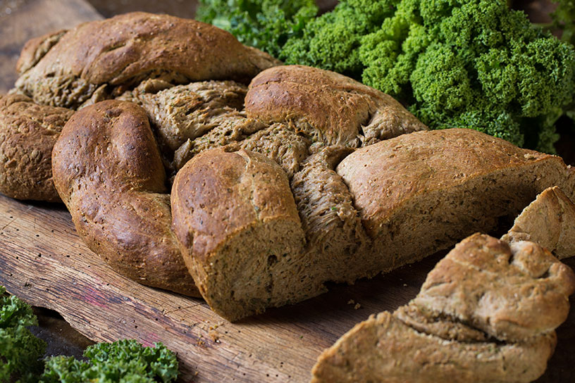 Grote stukken brood op een plank met boerenkool ernaast